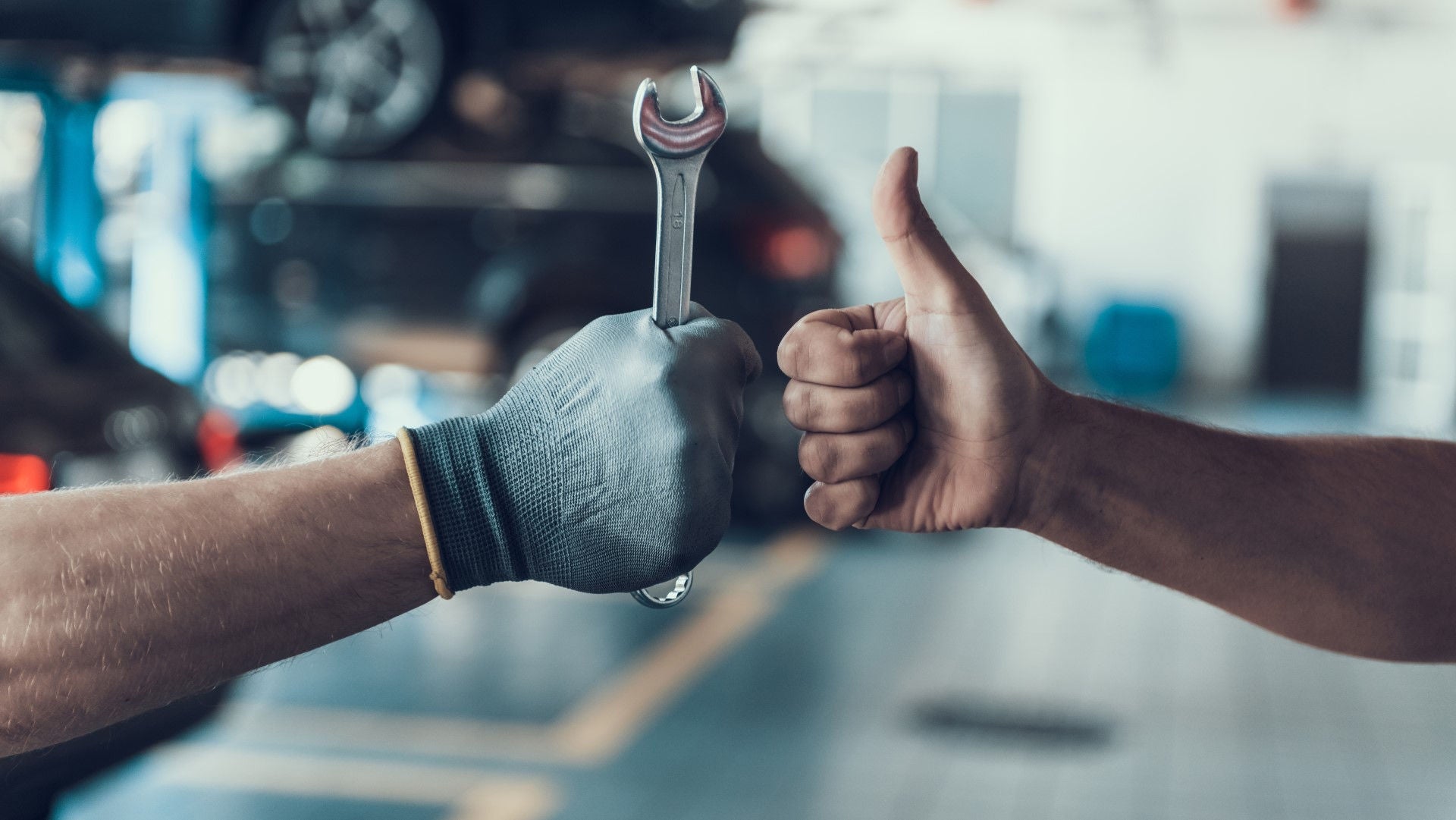 Two hands one with wrench one with thumbs up in a workshop