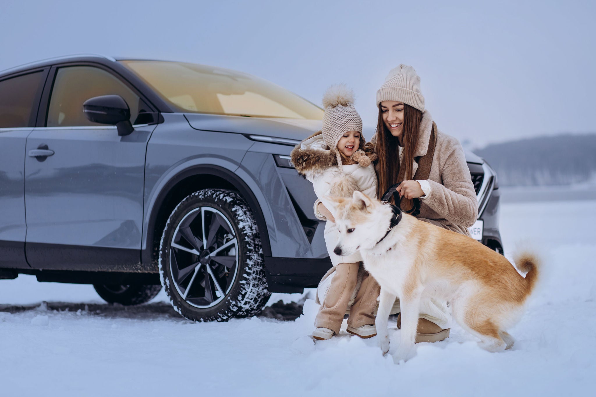 Woman with her daughter and dog having a walk in a snowy park by their car