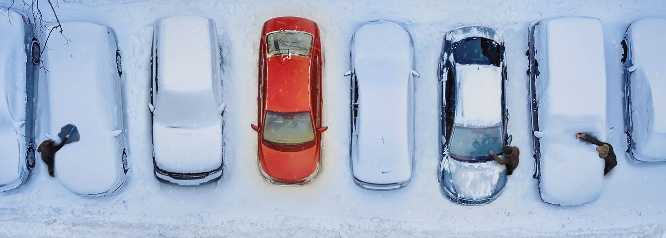 Zugeschneite Autos auf einem Parkplatz mit einem roten, nicht eingeschneiten Auto